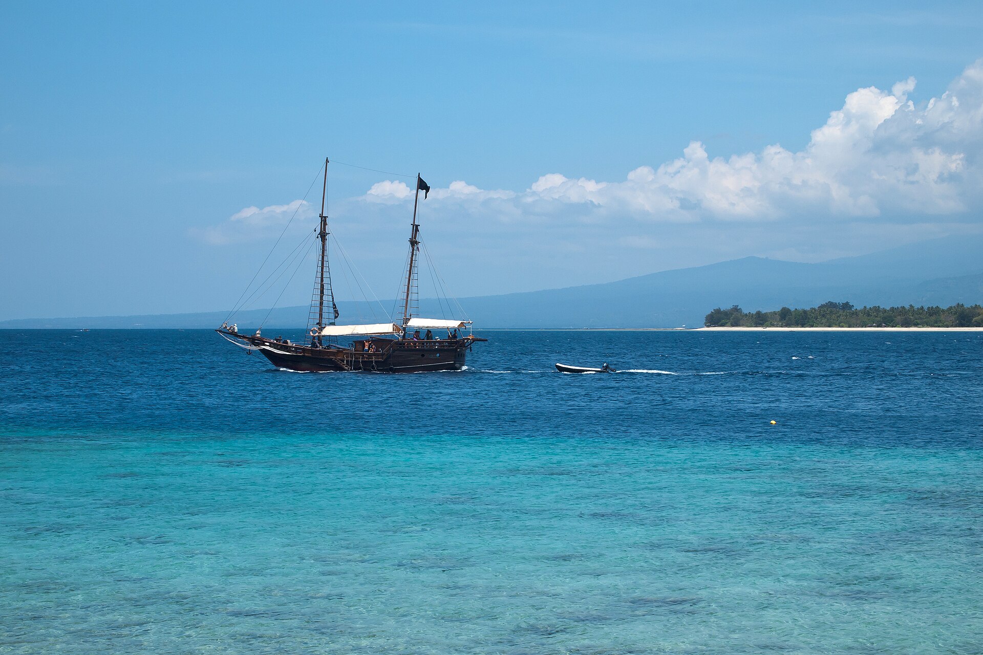 A traditional two-masted wooden sailing vessel on turquoise water off Gili Meno in the Bali Sea